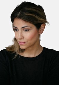 Pendientes de plata colgantes con un acento de perla redonda, llevados por una persona con una blusa negra, cabello castaño suave y ondulado, y maquillaje natural.