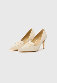 Beige pointed-toe high heels with a smooth texture, featuring a gold chain detail across the vamp and a slim heel.