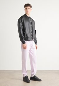 Sort faux læder bomberjakke med quiltet front, parret med lyse lilla joggers og sorte sneakers med hvide detaljer.