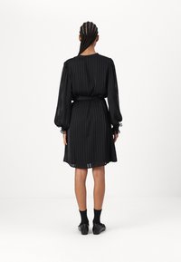 Črna nabrana obleka z dolgimi rokavi, pasom na pasu in prosojnimi manšetami. Tkanina ima gladko teksturo, kar daje tekoč silhueta.