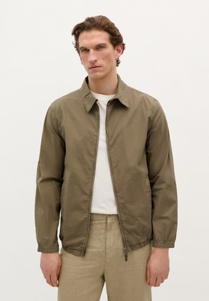 Khaki bomberjack met een rits aan de voorkant, een verspreid kraag en elastische manchetten. Draag het over een wit shirt, gecombineerd met lichtbeige broeken.