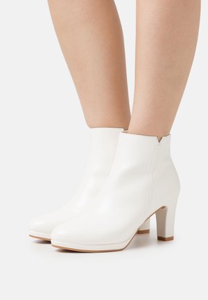 Bottes blanches jusqu'à la cheville à finition lisse, dotées d'un talon bloc, d'un bout pointu et de coutures latérales. Le design est épuré et minimaliste.