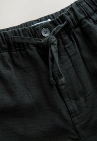 Pantaloni in tessuto nero strutturato con vita elasticizzata, chiusura con bottone nero e coulisse annodata sul davanti.