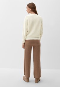 Cremefarvet ribstrikket sweater, afslappet pasform, lange ærmer. Kombineret med lysebrune vide bukser. Neutrale toner, blød tekstur og enkelt design.