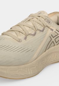 Gros plan d'une chaussure de course beige avec une semelle texturée, des lacets croisés et un motif à rayures sombres près du talon et du côté.