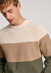 Suéter de punto con un diseño de bloques en tres colores: crema, beige y verde oliva, con costuras texturizadas y puños acanalados.