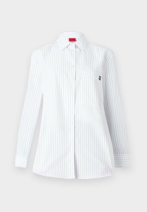 Bela srajca z dolgimi rokavi z modrimi vertikalnimi črtami, s koničastim ovratnikom, sprednjim žepom in majhnim vezenim logotipom na prsih.