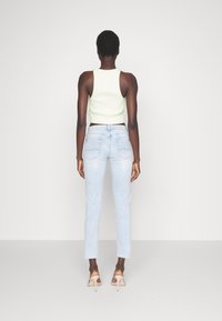 Hellgrünes, geripptes Cropped-Top, kombiniert mit hellblauen, geraden Jeans. Die Jeans haben eine ausgewaschene Textur und unversäuberte Säume.