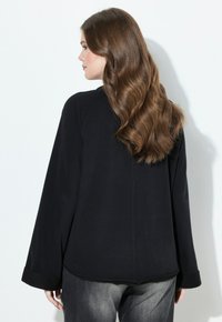 Maglione nero con vestibilità rilassata, maniche lunghe e orli rifiniti. Texture liscia con una leggera lucentezza; design semplice, senza motivi.