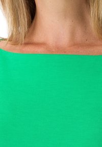 Zielony top z szerokim, prostym dekoltem, wykonany z miękkiego materiału. Tekstura jest gładka z lekkim streczem, podkreślająca intensywny kolor.