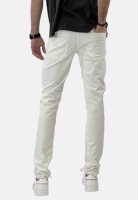 Pantaloni in denim bianco con vestibilità slim, caratterizzati da un design a quattro tasche e una leggera trama. Indossati con scarpe bianche, in piedi su uno sfondo semplice.
