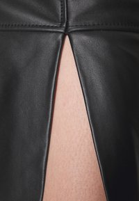 Zwarte leren rok met een verticale split die huid onthult. De textuur lijkt glad met subtiele stiksels rond het splitgebied.