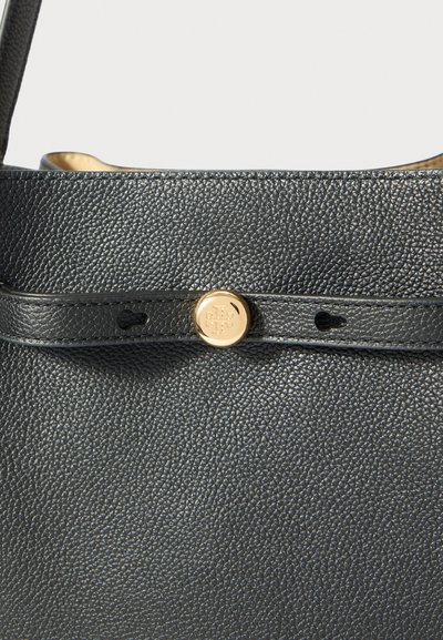 Fekete textúrájú bőr kézitáska rész, vékony pánttal és egy középen elhelyezkedő, logóval gravírozott, kerek arany gombbal.