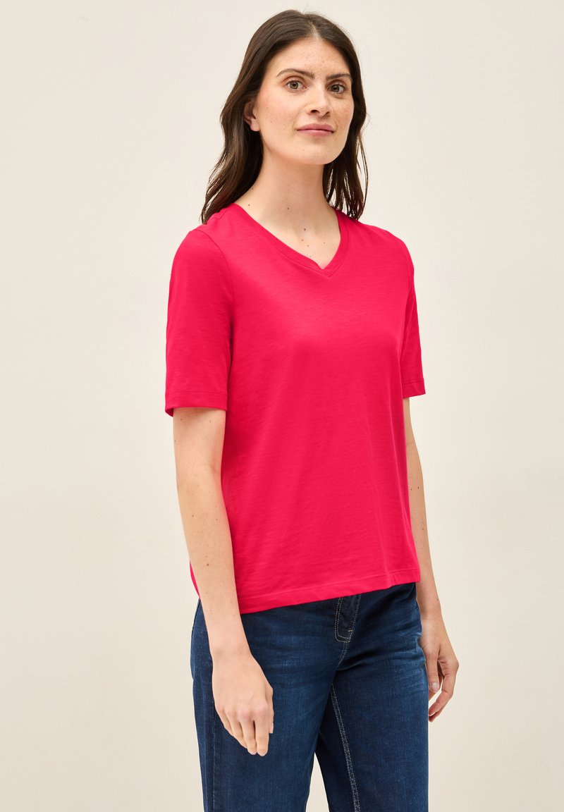 V-hals, kortærmet t-shirt i lys pink stof, med en afslappet pasform og glat tekstur, kombineret med mørkeblå jeans.