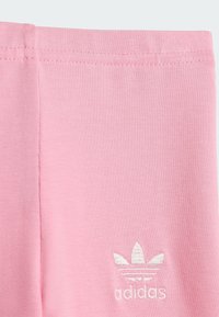 Ružové bavlnené legíny s hladkým textúrou, obsahujúce vyšitý biely logotyp Adidas pri leme a priliehavý elastický pás.