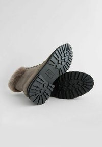 Graue Wildleder-Stiefeletten mit einem Pelzkragen, ausgestattet mit einer gezahnten schwarzen Gummisohle und einem geprägten Logo auf der Außensohle.