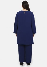 Navyblaues Langarm-Oberteil mit einem Keyhole-Rücken-Detail, kombiniert mit passenden weit geschnittenen Hosen. Weicher, strukturierter Stoff und lässige Passform.