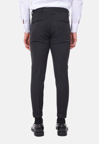 Pantaloni neri sartoriali con una vestibilità slim, dotati di tasche posteriori, una texture liscia e risvolti, abbinati a scarpe da uomo nere.