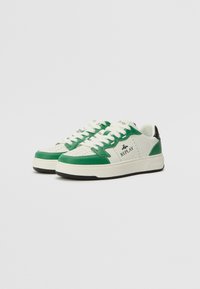 Grønne og hvite sneakers med en glatt lærfinish, med perforeringer, hvite snøringer og svarte detaljer på hælen.