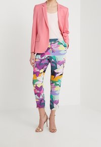 Różowa marynarka na lekkim topie, zestawiona z kwiecistymi spodniami w odcieniach fioletu, zieleni i żółci. Całość dopełniają złote sandały na cienkich paskach.