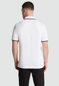 Witte polo met een kraag, met donkerblauwe afwerking op de mouwen. Katoenen materiaal, eenvoudig ontwerp met een rechte snit.