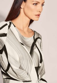 Schwarz-weiß gemusterte Bluse mit abstrakten Wirbeln, Rundhalsausschnitt und glattem, leichtem Stoff. Verfügt über dezente Drapierungen und Schulterakzente.