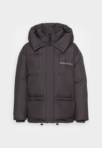 Svart puffjacka med hög krage, framdragkedja och två fickor med dragkedja. Mjuk, kviltad textur med Calvin Klein Jeans-logotyp på bröstet.