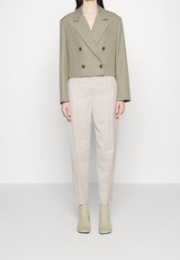 Zkrácený olivově zelený blazer s dvojřadovým zapínáním, v kombinaci s světle béžovými kalhotami s vysokým pasem a světle texturovanými ponožkami.