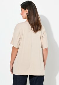 Beige kortærmet skjorte lavet af blødt stof, med en afslappet pasform og diskret midtersøm detaljer, sammen med mørke denim jeans.