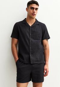 Black short-sleeve shirt and matching shorts made of textured fabric. Features a collar, button front, and a chest pocket.
