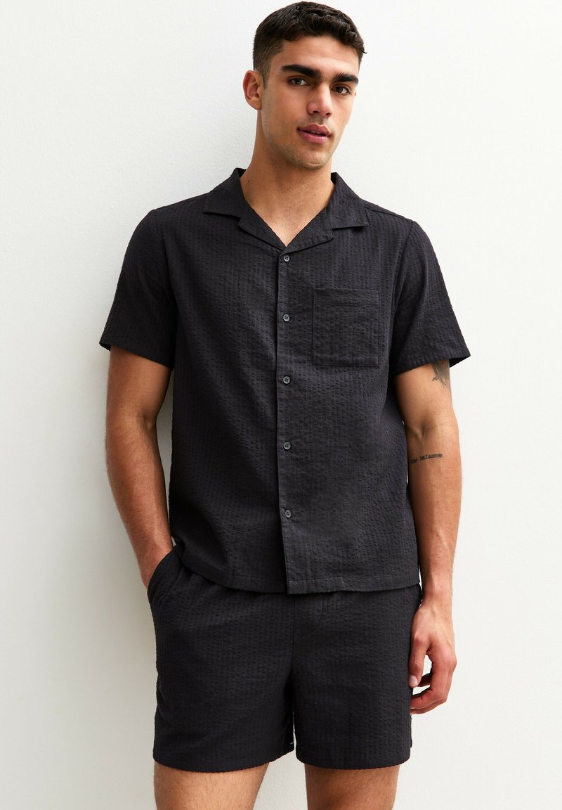 Black short-sleeve shirt and matching shorts made of textured fabric. Features a collar, button front, and a chest pocket.