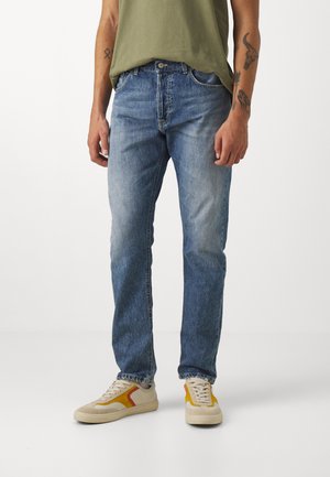 Jeans in denim azzurro chiaro con una vestibilità rilassata, caratterizzati da una vita a mezza altezza, cinque tasche e una leggera scoloritura, abbinati a sneakers beige.