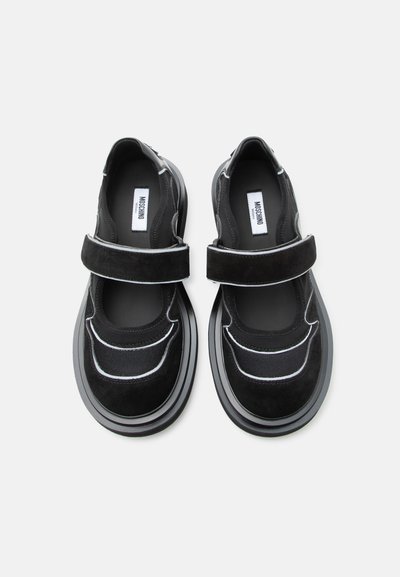 Paire de chaussures noires de style Mary Jane avec semelles épaisses et bandes Velcro, présentant des textures en mesh et en daim ainsi que des accents de passepoil blanc.