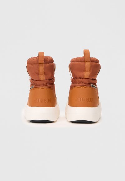 Brązowe ocieplane botki za kostkę ze skórzaną piętą, białą podeszwą i pętlą do zakładania. Na tyle tłoczone "MOON BOOT". Minimalistyczny design.