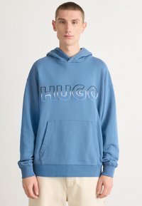 Felpa blu con tasca kangaroo frontale, caratterizzata dalla scritta "HUGO" in grassetto e con lettering a contrasto. Realizzata in morbido tessuto testurizzato.