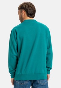 Tyrkis crew neck sweatshirt med lange ærmer, en glat tekstur og ribbede manchetter. Sammen med blå denim jeans for kontrast.