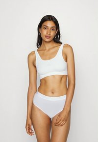 Λευκό αθλητικό σουτιέν χωρίς ραφές και ταιριαστό σλιπ με ψηλή μέση, κατασκευασμένα από λεία ύφασμα με ελαστική εφαρμογή και διακριτικές λεπτομέρειες λογότυπου.