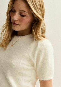 Wit, kort mouwensweater van zacht, pluizig materiaal met een ronde halslijn en een delicate afwerking. Heeft een subtiele glans en een lichtgewicht ontwerp.