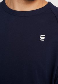 Mörkblå T-shirt i bomull med rund halsringning. Har en liten vit logotyp på bröstet. Slät textur och korta ärmar.