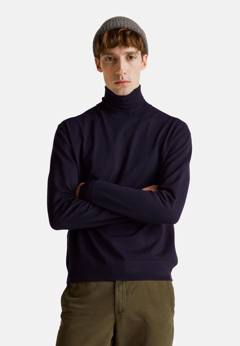 Marineblauer Rollkragenpullover aus weichem Strickmaterial, mit langen Ärmeln und einer taillierten Silhouette, kombiniert mit olivgrünen Hosen.