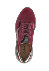 Red suede sneaker with textured upper, gray accents, rounded toe, and flat laces. Cushioned insole visible with branding inside.