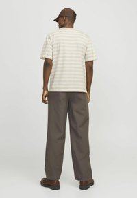 Camisa corta de manga larga a rayas beige, de corte relajado, combinada con pantalones anchos marrones oscuros y zapatos marrones, vista desde la parte posterior.