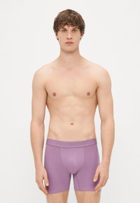 Boxers roxos feitos de um tecido macio com um ajuste justo. Apresentam uma cinta com logotipo e um bolso frontal para suporte.