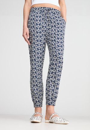 Pantaloni jogger blu navy con motivo floreale bianco, vita elastica, tasche laterali e polsini affusolati. Abbinati a scarpe slip-on con perline.
