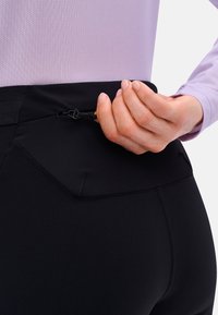 Schwarze Sporthosen verfügen über einen strukturierten Bund mit einem Kordelzug. Das Material ist glatt und dehnbar, entworfen für Komfort und Flexibilität.