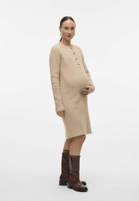 Robe en tricot côtelé beige avec des manches longues et des boutons marron, longueur genou, associée à des bottes en cuir marron montantes.