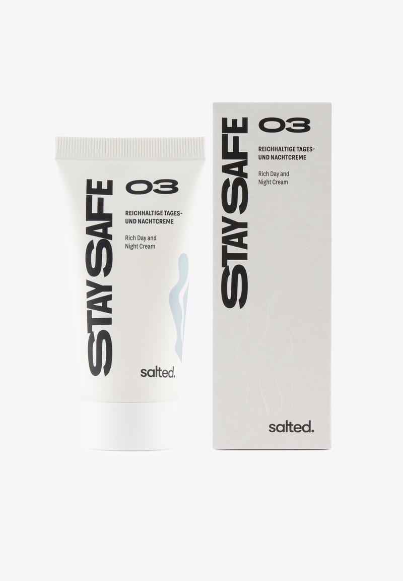 Tubo bianco con un tappo texturizzato, etichettato "STAY SAFE O3," accanto a una scatola bianca con un design minimalista e testo nero che indica "Crema Ricca Giorno e Notte."