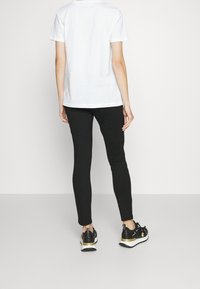 Svarta leggings med en figurnära design, matchade med en enkel vit t-shirt. Outfitten kompletteras av svarta och guldiga träningsskor.