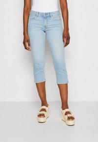 Vaalean siniset vaaleat farkkutrikoot sisältävät perinteisen viiden taskun muotoilun ja keskikorkean vyötärön, yhdistettynä vaalean kermanvärisiin platform-sandaaleihin.