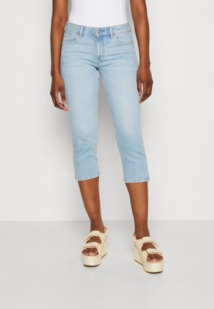 Ljusblå beskurna denimjeans har en traditionell femfickorsdesign med midjehöjd, åtföljda av krämfärgade platåsandaler.